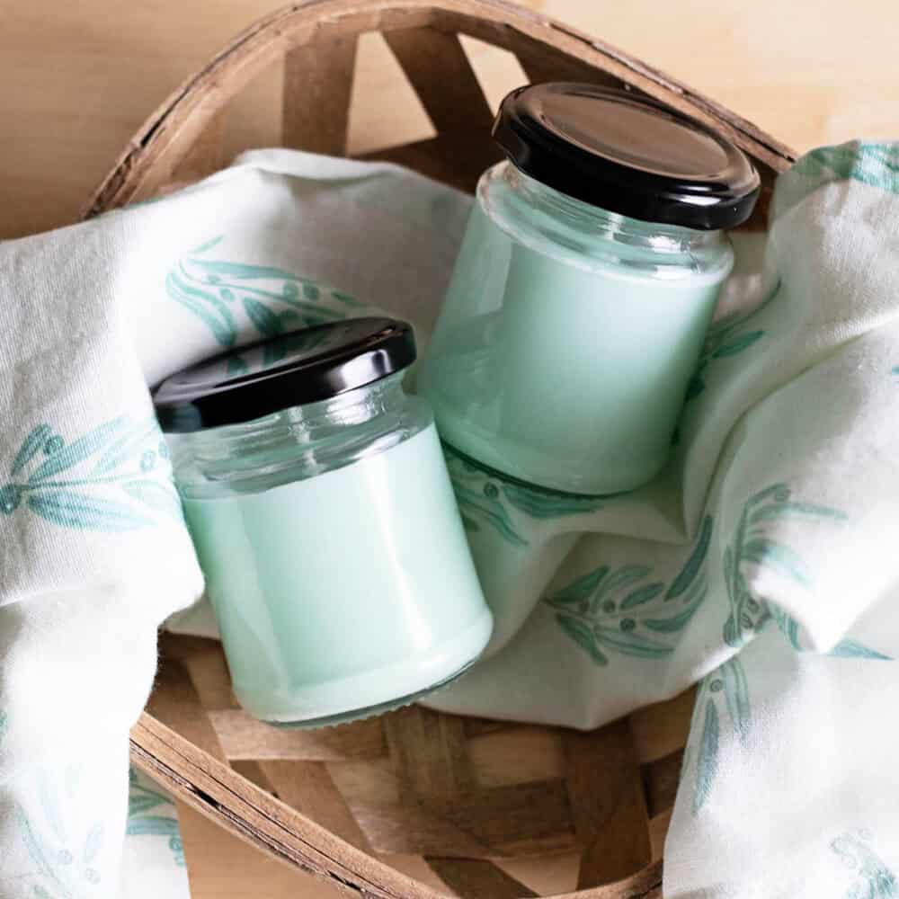 Basket filled with tea towel and jars of candles with a mint color.