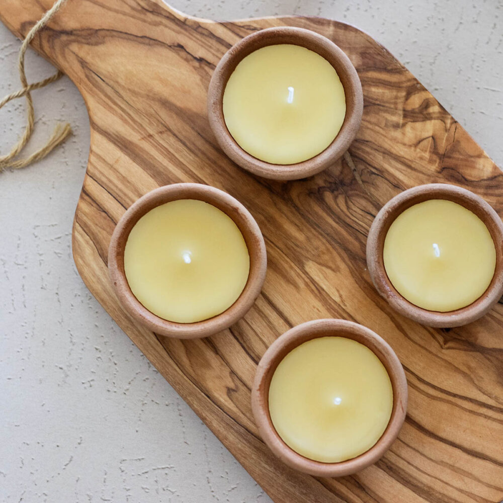 Terracotta candle bowls filled with hand poured beeswax candles on a olive wood board and rustic stucco counter outdoors.