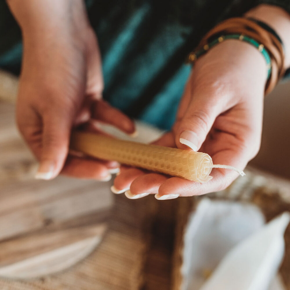 Holding a hand rolled beeswax taper candle in hands over a craft table with supplies.