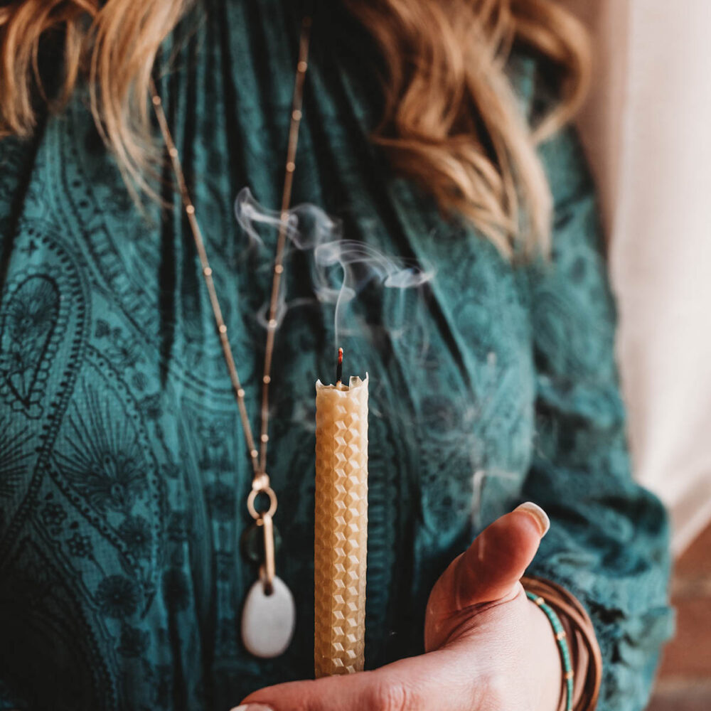 Holding a beeswax candle in taper in hands with smoke snaking above the wick after putting it out.