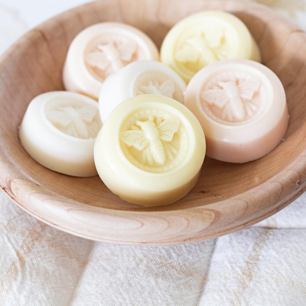 Handmade round soaps embossed with honey bees in a natural wood bowl.